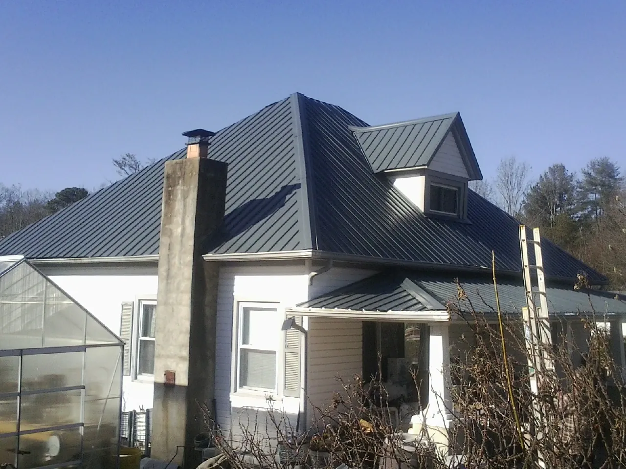 Dark blue standing seam metal roof on a white farmhouse with dormer — Slate & Tile Roof Repair by Roofing Brothers in Anamosa