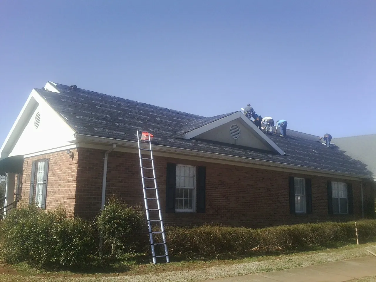 Crew tearing shingles off a brick ranch roof with a ladder set — Emergency Roof Repair work by our crew in Anamosa