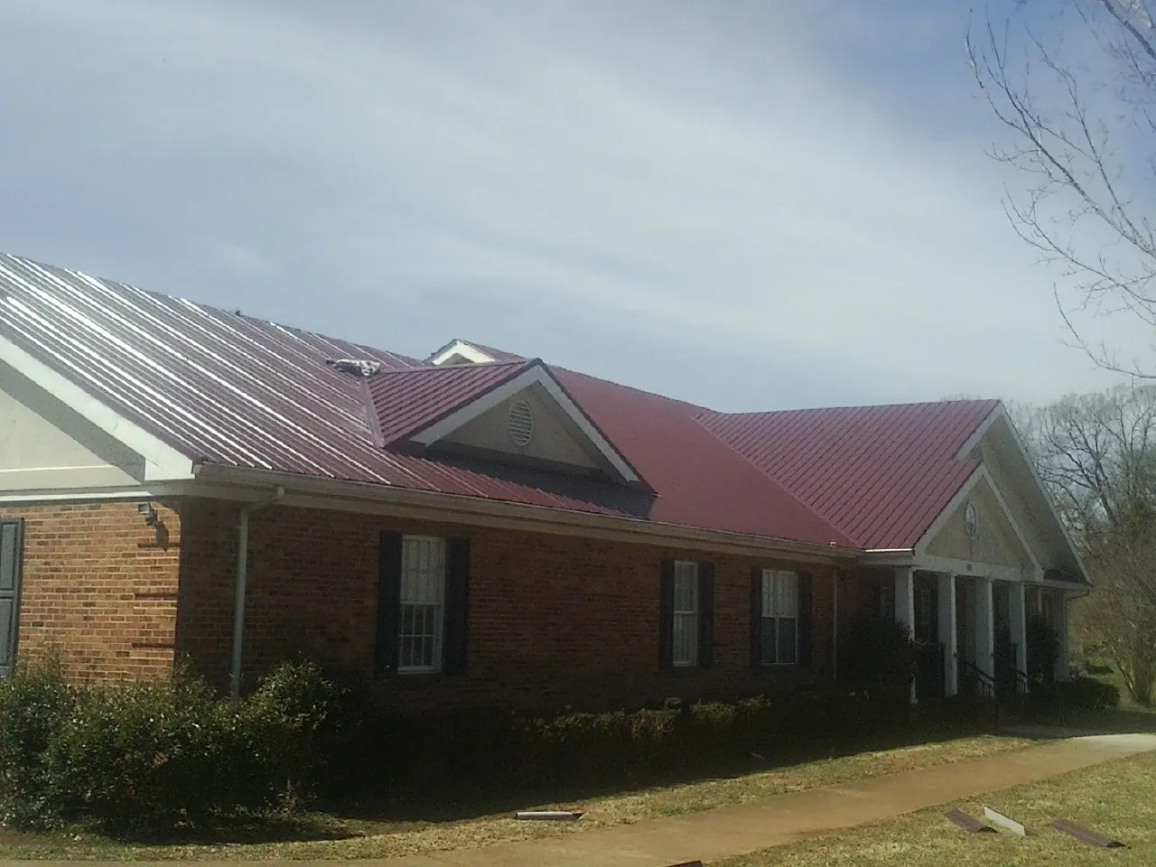 Red metal roof with gabled entries on a long brick building, from a Hail Damage Roof Repair job in Anamosa