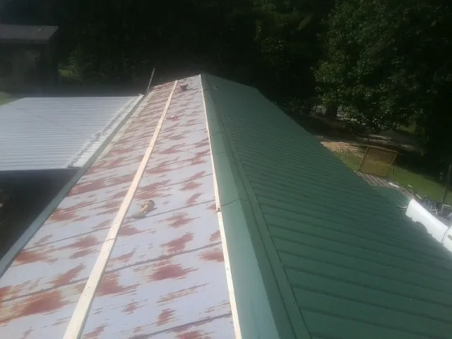 Old rusted panels beside newly installed green metal roofing — Wind Damage Roof Repair by Roofing Brothers in Anamosa
