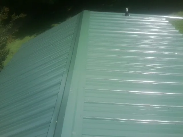 New green metal panels meeting at the ridge of a roof — Flat Roof Repair work by our crew in Anamosa