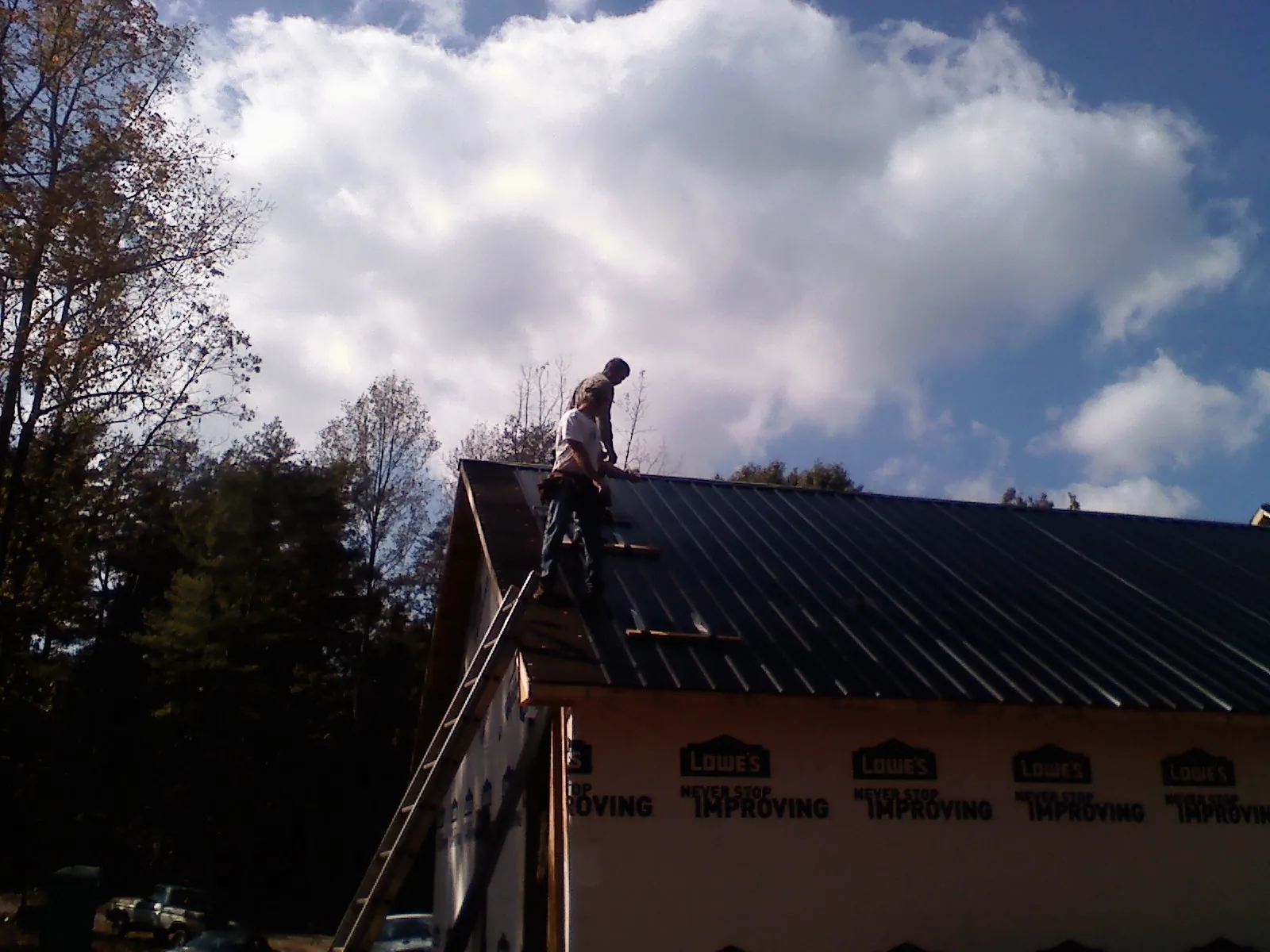 Roofer fastening dark metal panels high against a cloudy sky, from a Roof Inspection job in Anamosa