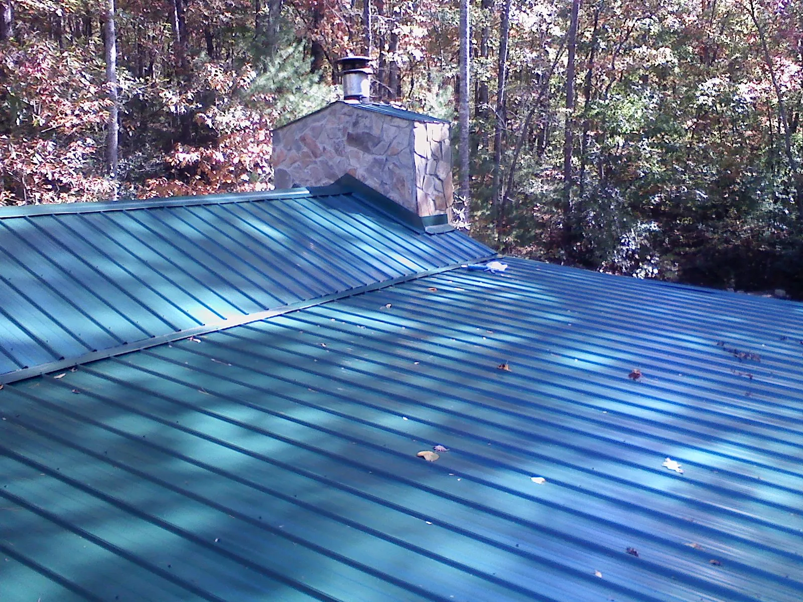 New green metal roof and stone chimney surrounded by autumn woods in Anamosa