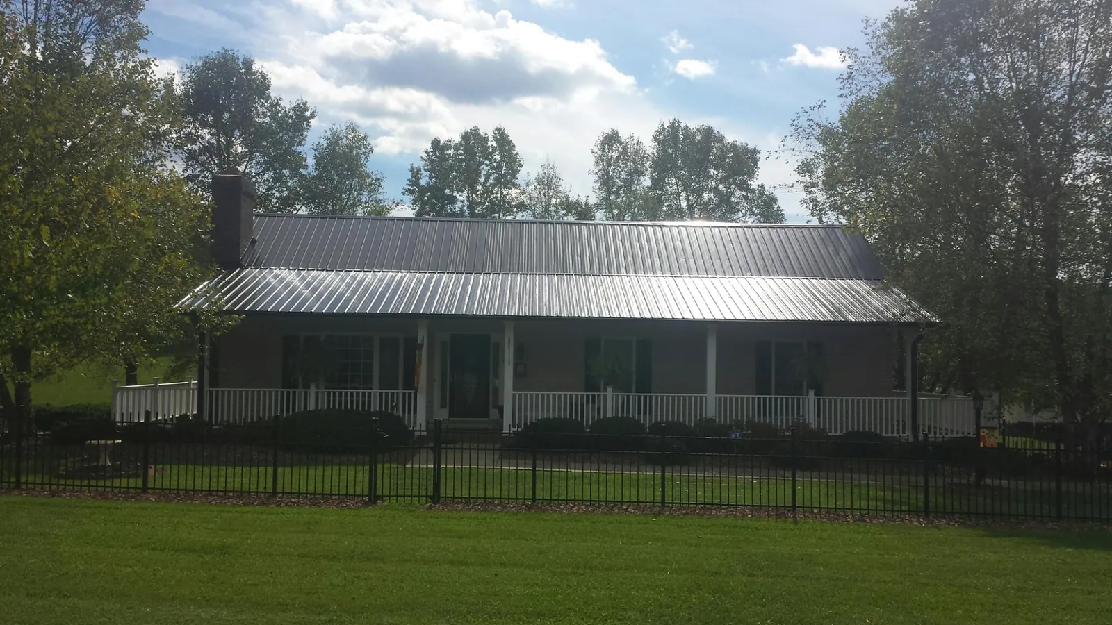 Gray metal roof on a brick ranch with a full width front porch — Gutter Guard Installation work by our crew in Anamosa