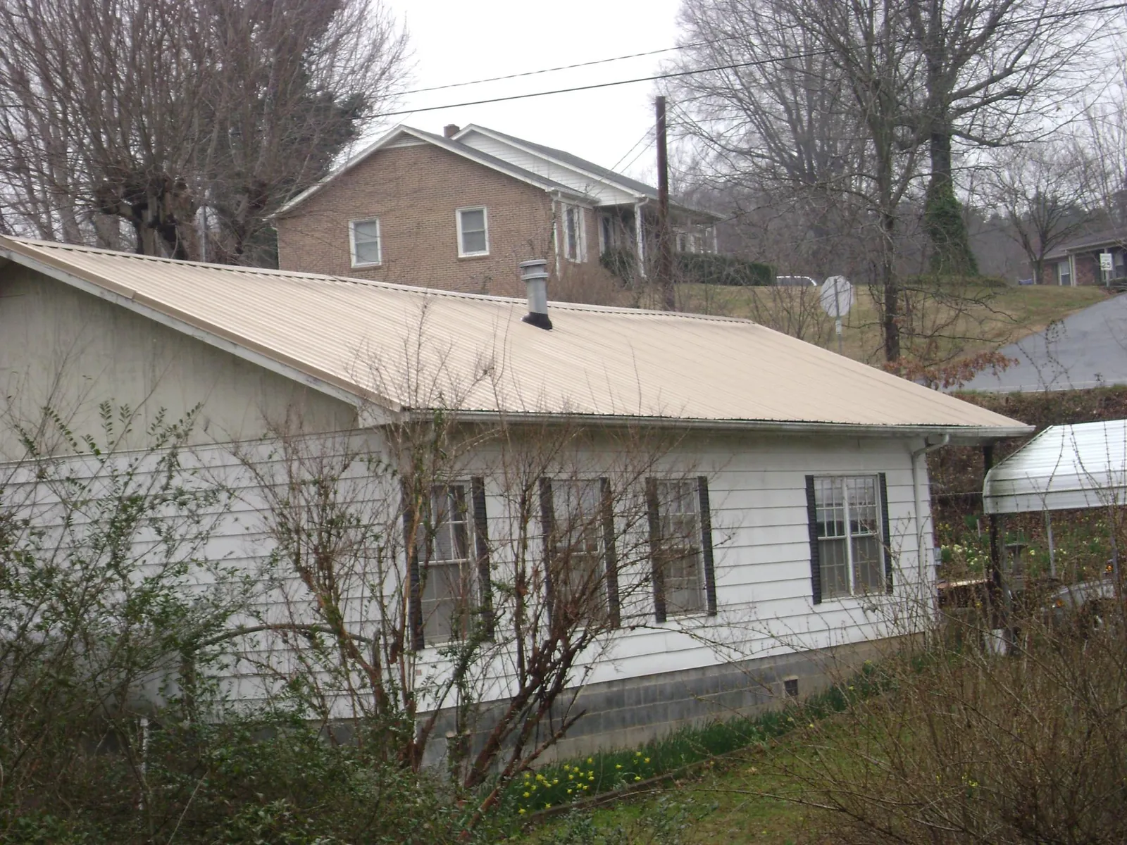 Tan metal roof on a white sided house set into a hillside — Commercial Roofing by Roofing Brothers in Anamosa