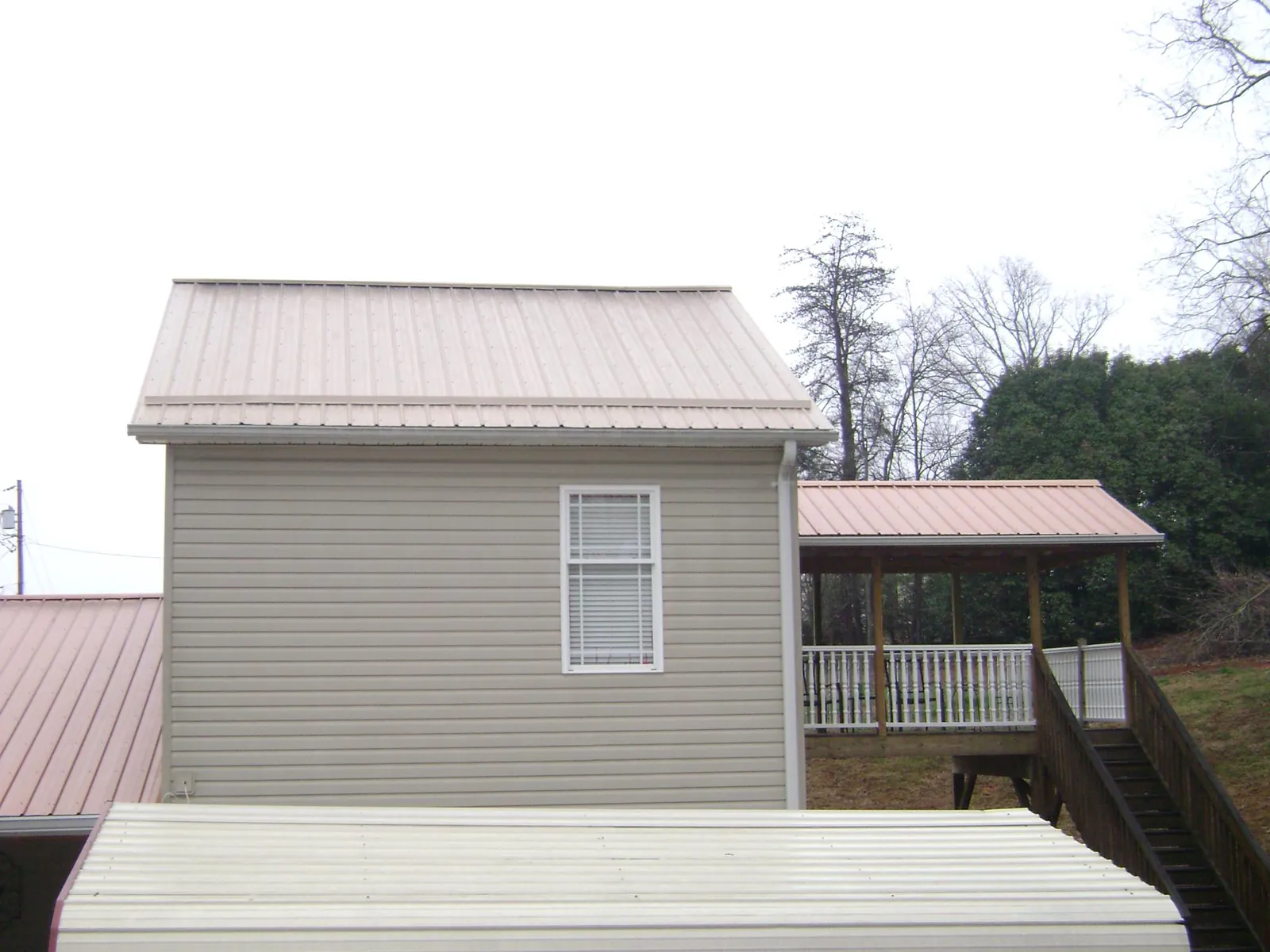 Tan metal roofs on a two story addition and attached porch, from a Roof Replacement job in Anamosa
